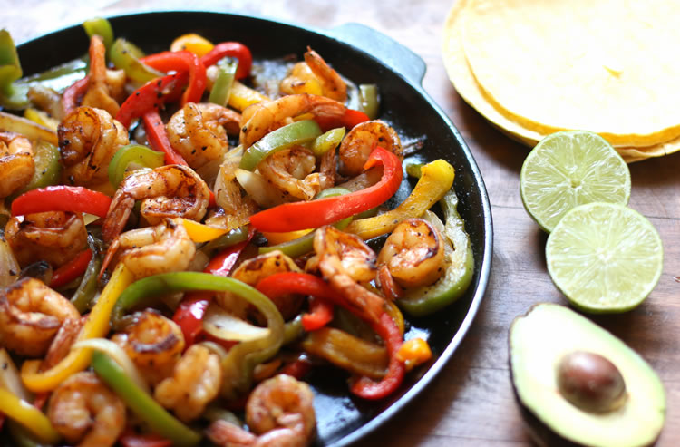 Fajitas aux crevettes faciles à faible teneur en glucides sur une poêle à côté de citron vert et d'avocat