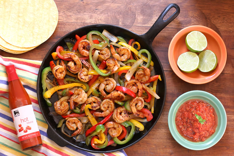 fajitas aux crevettes faciles sur une poêle à côté de tranches de citron vert et de salsa