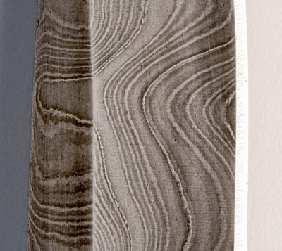 Une section d'une lame de couteau avec divers motifs superposés gris argenté et noir dans le métal.