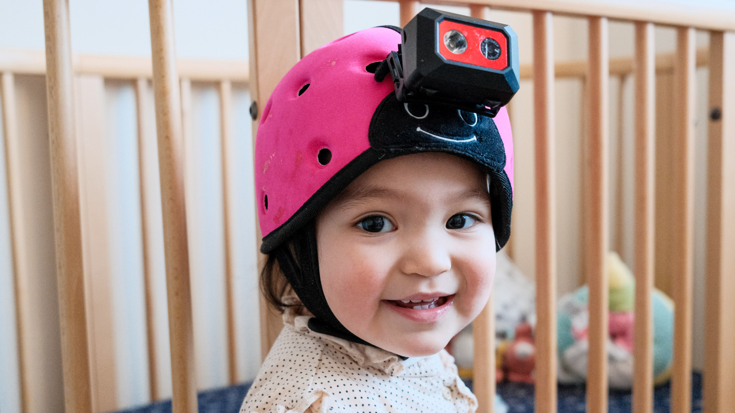 gros plan d'un bébé souriant portant un casque-caméra avec les barreaux d'un berceau en arrière-plan