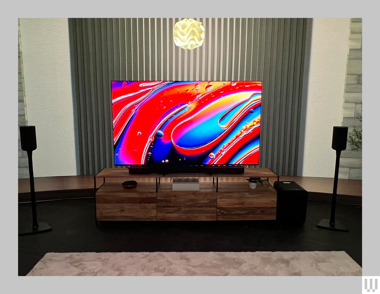 Téléviseur à écran plat mince sur crédence marron avec des illustrations rouges abstraites sur l'écran, de petits haut-parleurs sur des supports de chaque côté et un...