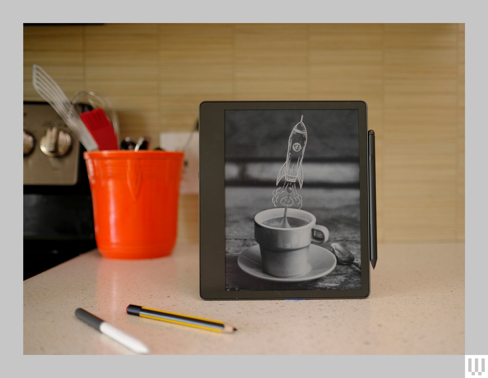 Tablette noire posée sur le comptoir de la cuisine avec le dessin d'une tasse à café et d'une fusée sur l'écran et des stylos numériques devant