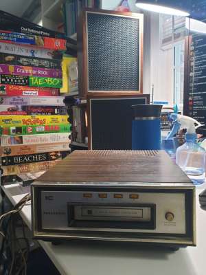 Un petit lecteur 8 pistes et des haut-parleurs tout aussi petits, ainsi qu'une pile de cassettes VHS. 
